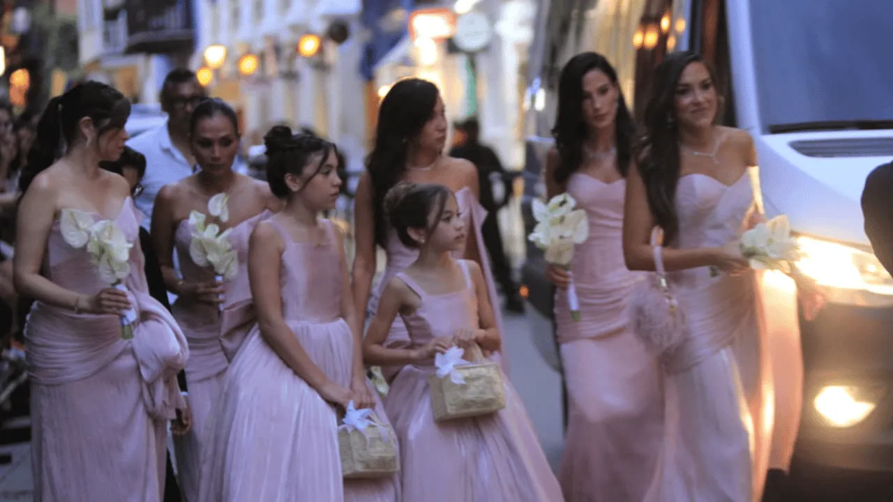 Mujeres y dos niñas con vestidos largos rosados sostienen cartuchos blancos y canastas.